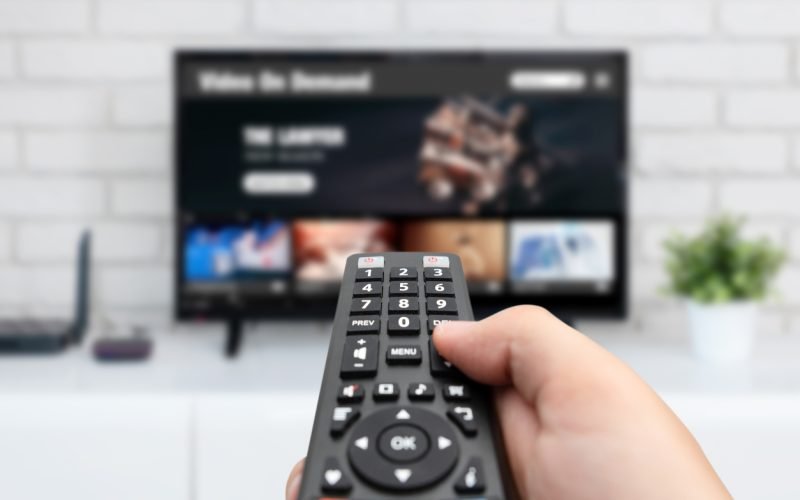 Man watching TV, remote control in hand. VOD service on TV