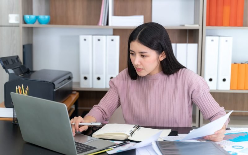 Young pretty woman working with laptop computer on table in the office, She checking paperwork together